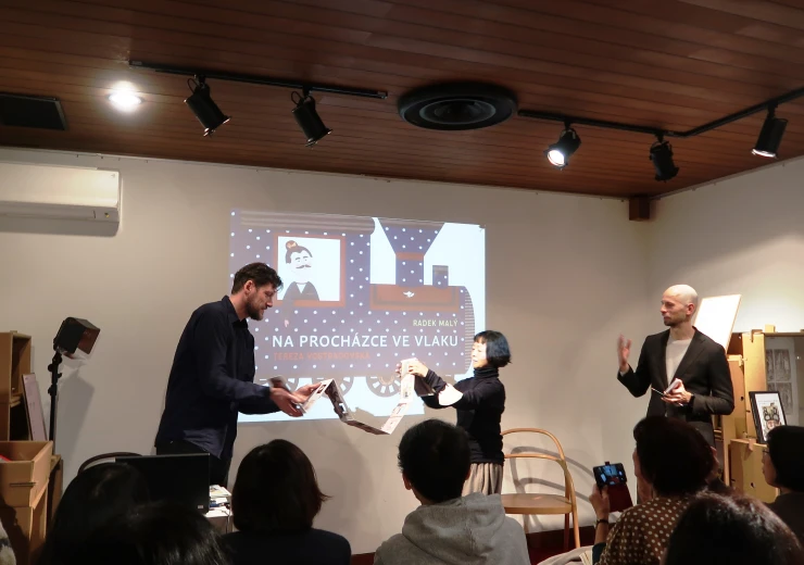 Autor Radek Malý za pomoci Iku Dekune a zástupců Českého centra Tokio předvádí účastníkům besedy své leporelo 
